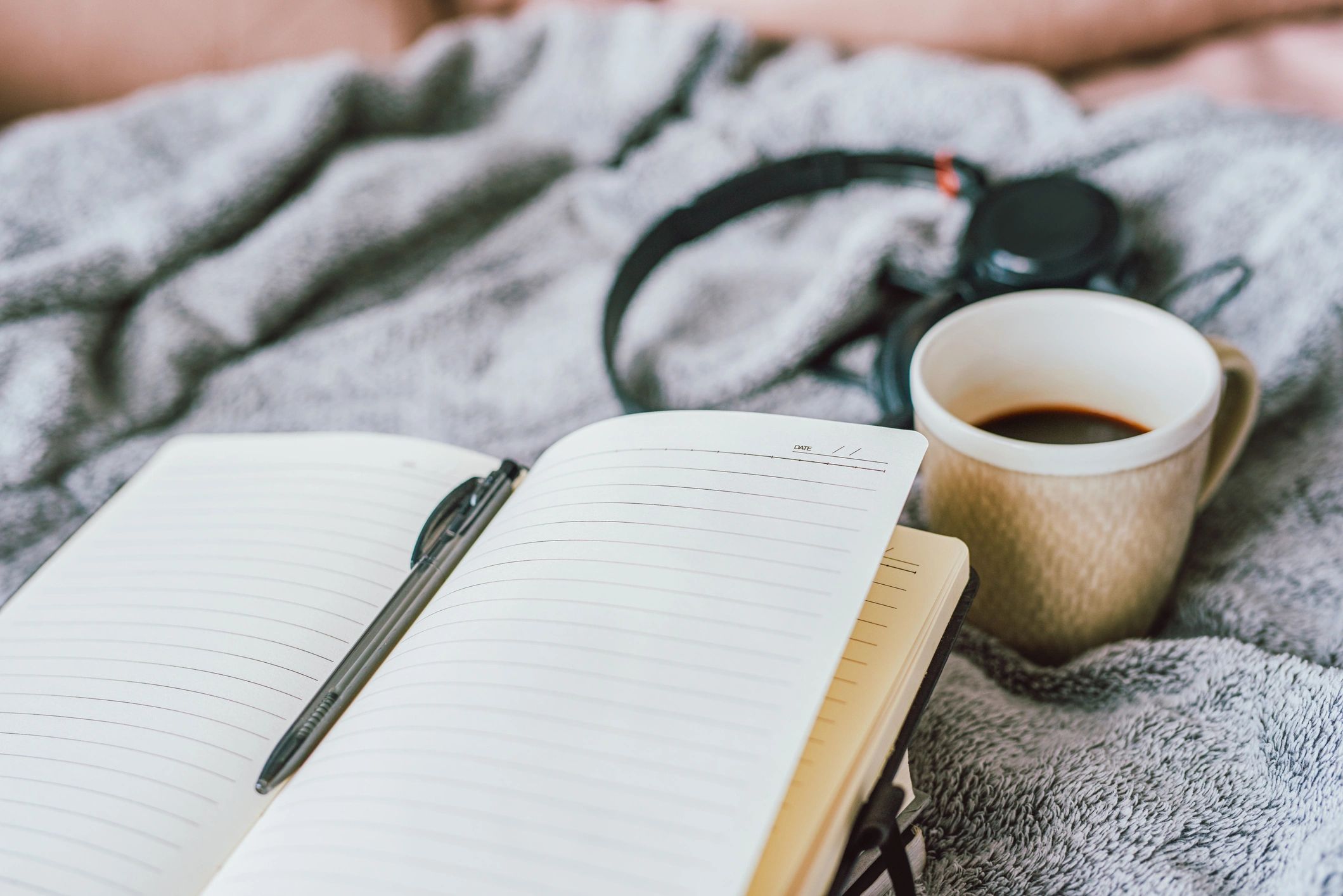 Notebook and coffee on a bed, suggesting reflection and journaling