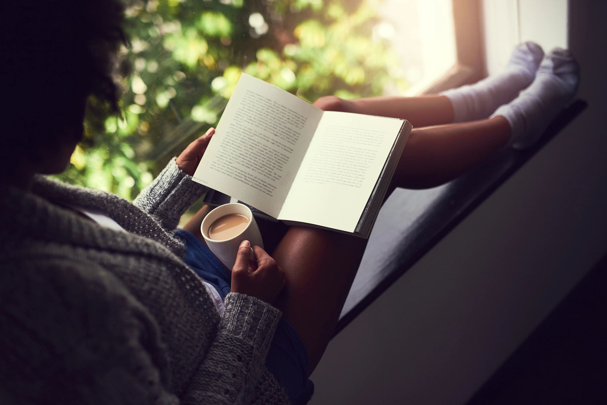 Person reading a book while enjoying a cup of coffee at home